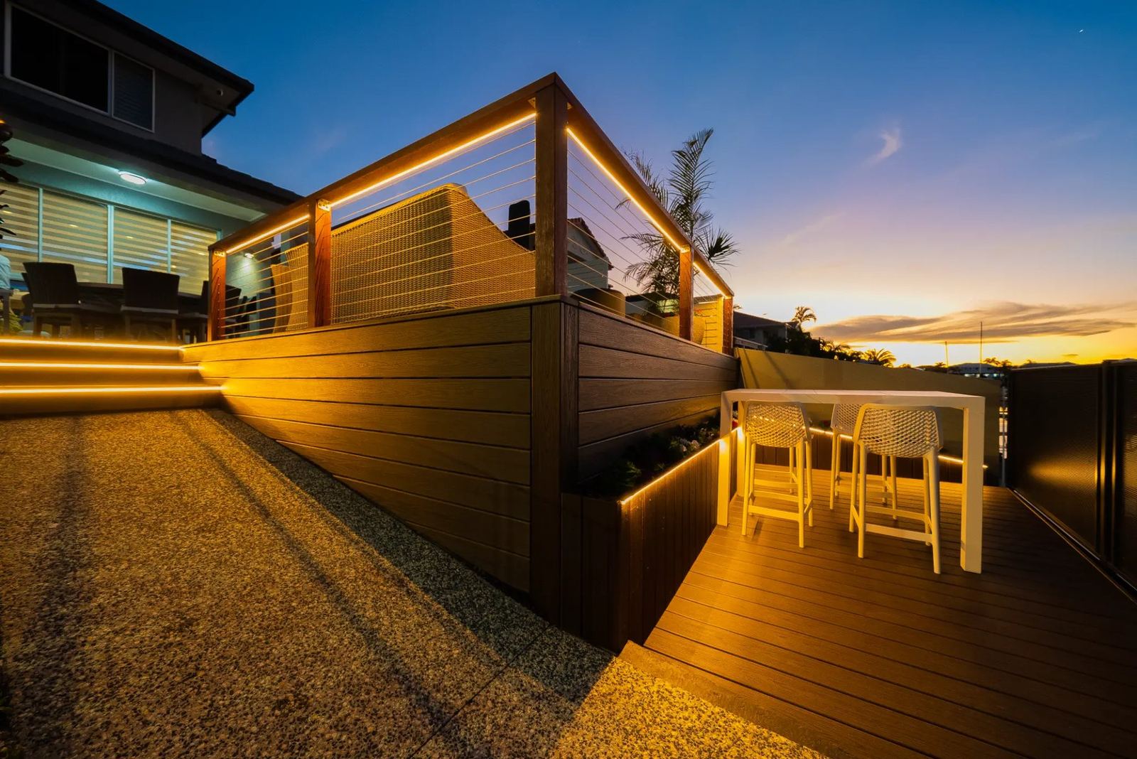 A composite deck with integrated lighting and glass balustrade at dusk, overlooking a canal.